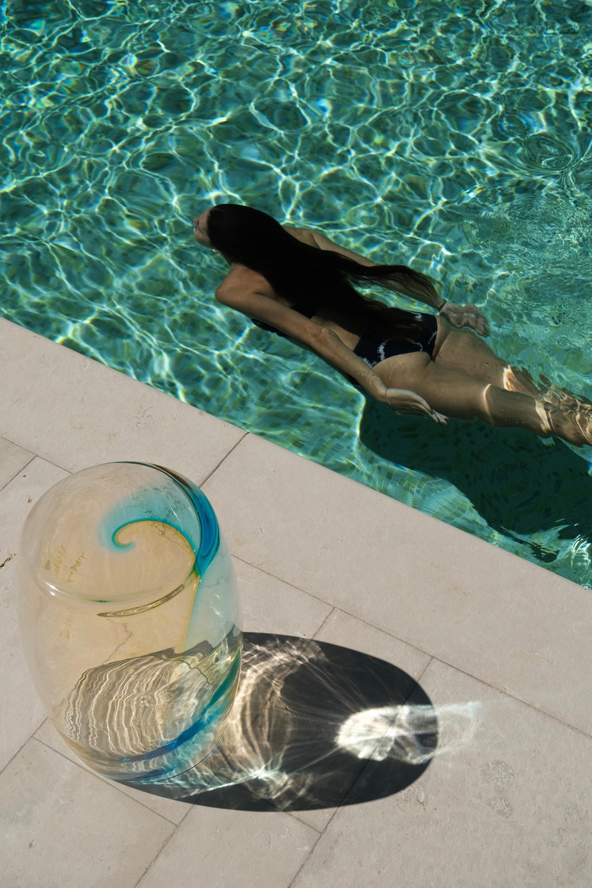 Tavolino Ambra Marina 50 Murano glass table photographed poolside with strong light refractions and aquamarine colour gradient.