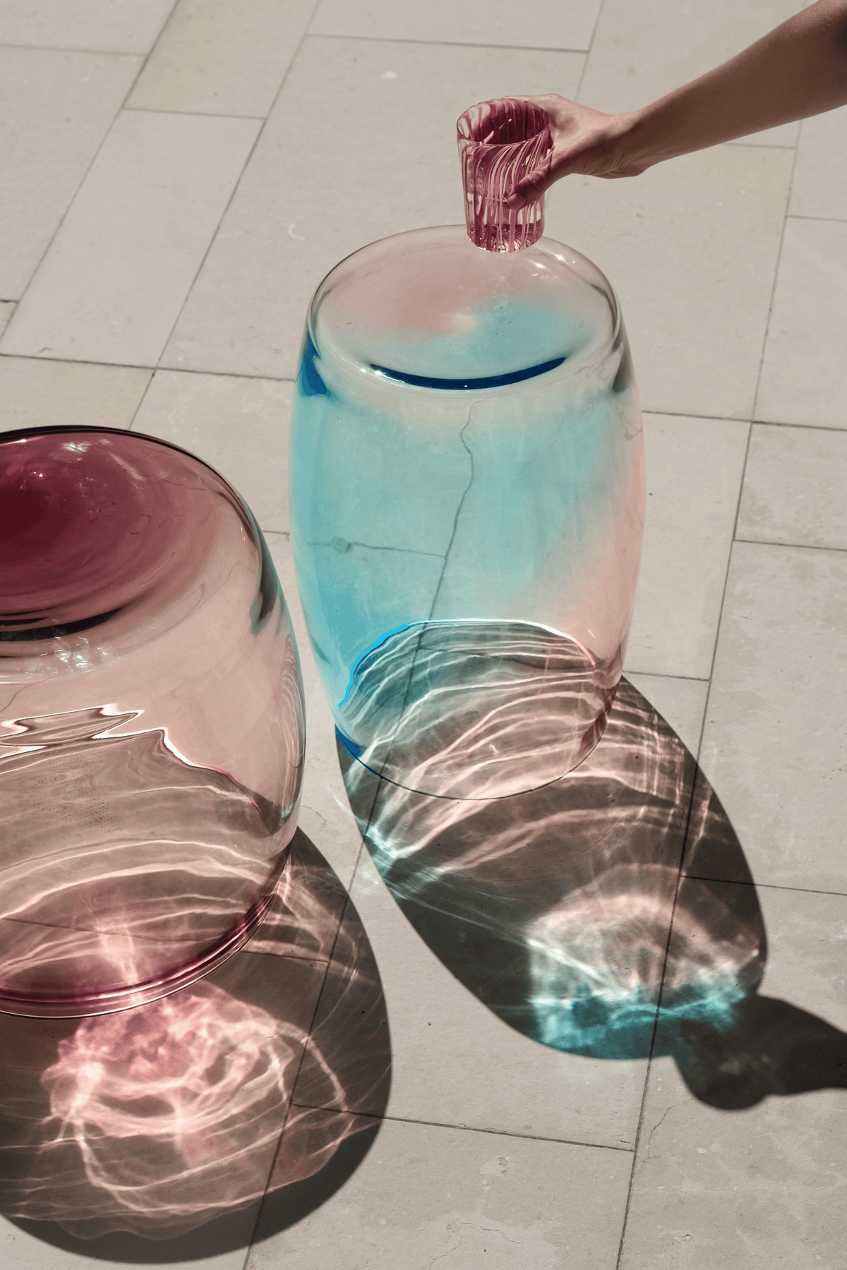 Tavolino Sirena 50 beside a pool — Murano glass table casting coloured reflections in sunlight.
