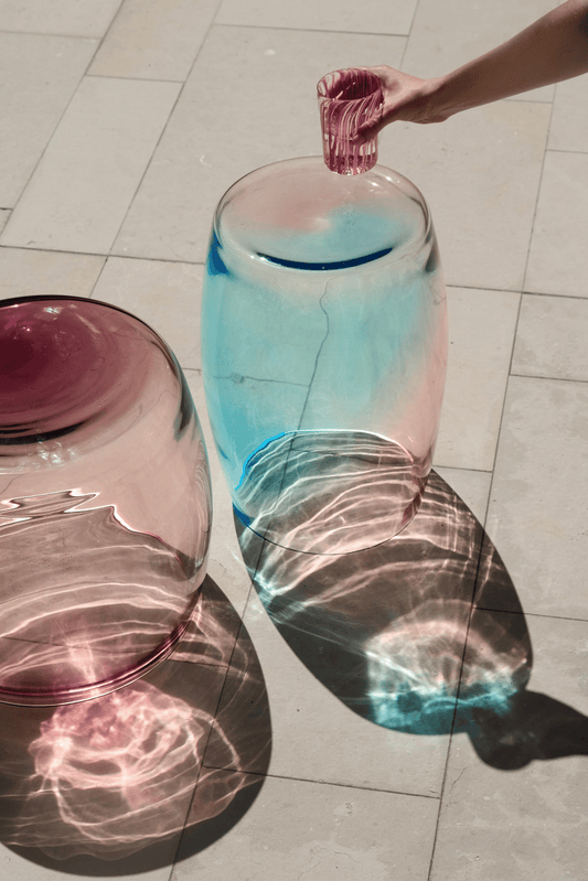 Tavolino Sirena 50 beside a pool — Murano glass table casting coloured reflections in sunlight.