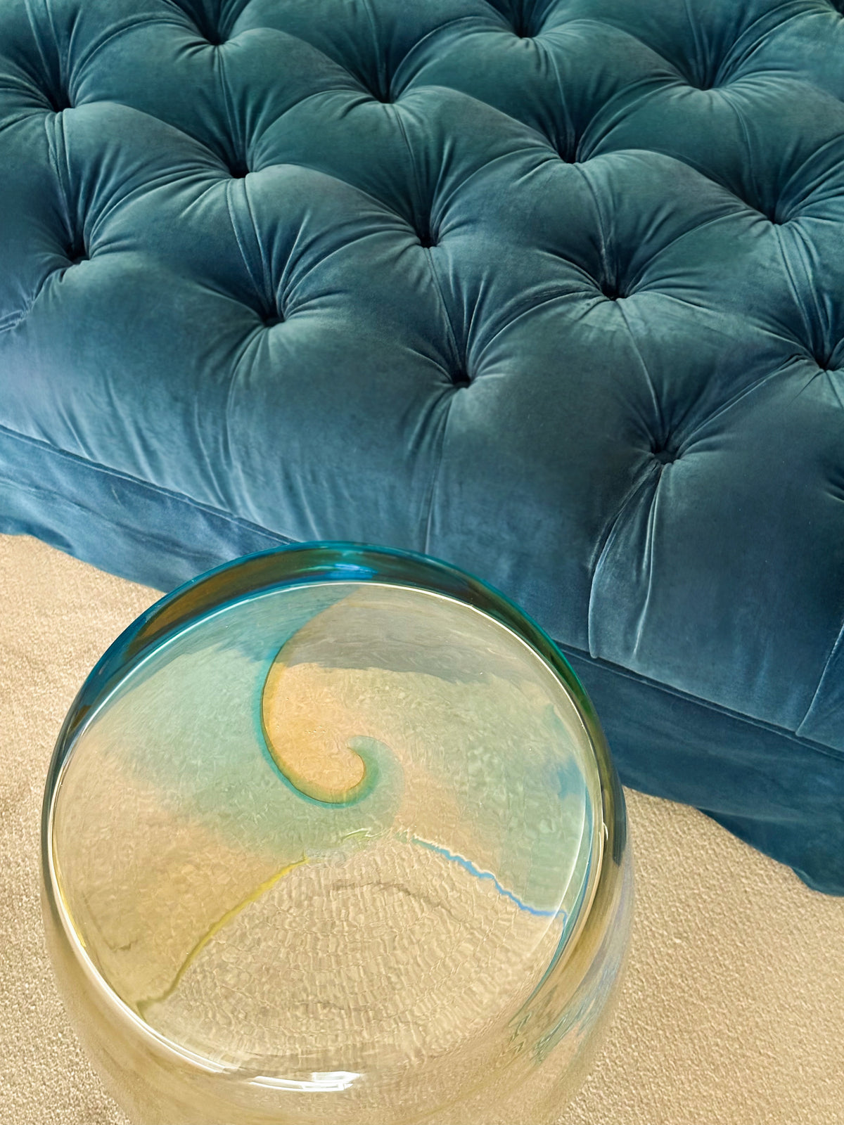 Tavolino Ambra Marina 50 hand-blown Murano glass table styled beside a blue velvet sofa, showing aquamarine gradient and sculptural form.